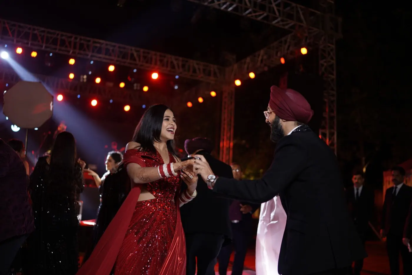 A couple dancing among guests beneath warm red stage lights